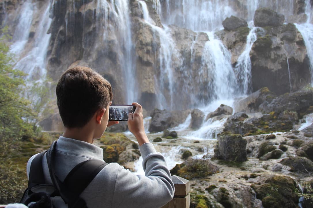 A traveler photographing a broad mountain waterfall